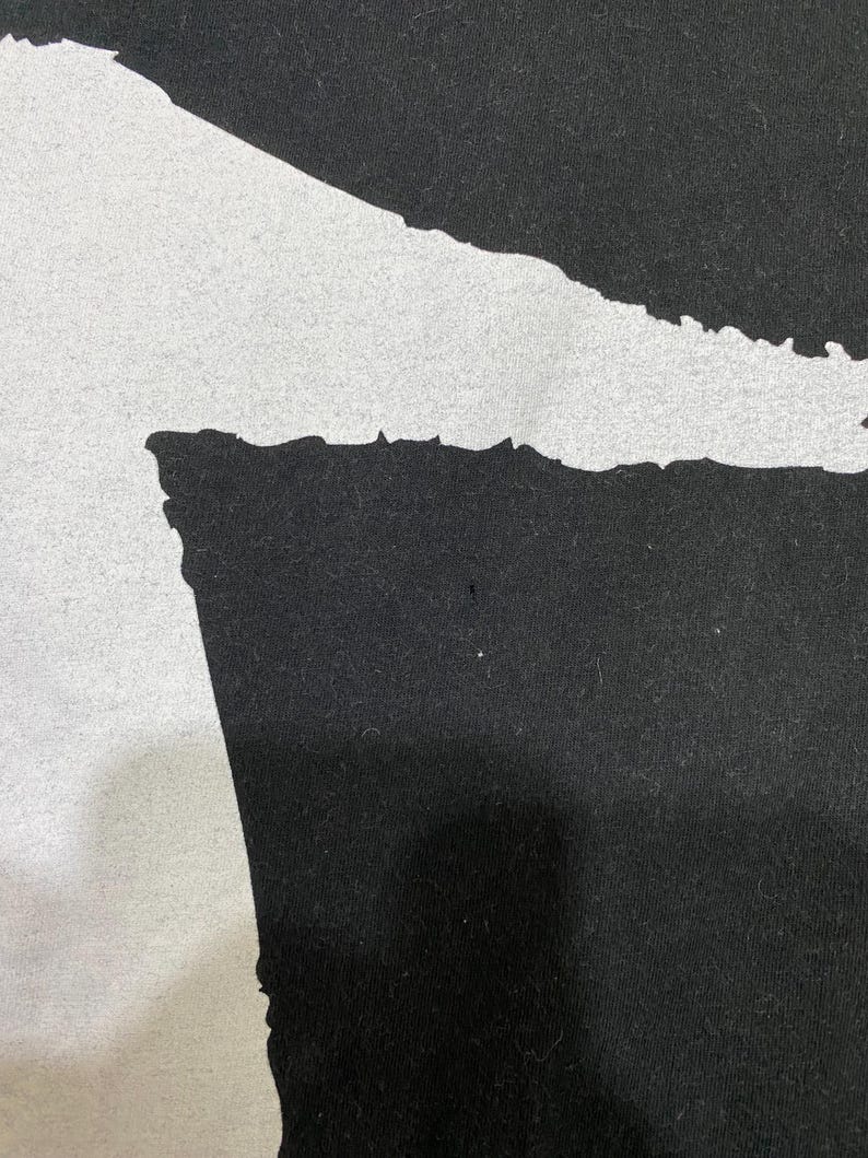 Puede incluir: Primer plano de una tela negra con una forma abstracta blanca grande. La forma tiene un borde rugoso y texturizado, que contrasta con el fondo negro liso. La imagen est&aacute; bien iluminada, destacando los detalles de la tela.