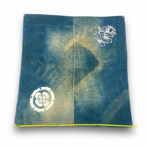 May include: A blue and white fabric square with a white floral design and a white geometric design. The fabric has a faded, vintage look.