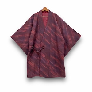Peut inclure: Un kimono bordeaux avec un motif de coups de pinceau diagonaux. Le kimono a de larges manches et une fermeture à nouer à la taille. Le vêtement est présenté sur un cintre en bois sur fond blanc.