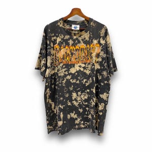Peut inclure: T-shirt tie-dye noir et blanc avec un logo "Backdraft" orange et jaune avec des flammes. Le logo comprend également le texte "Universal Studios".