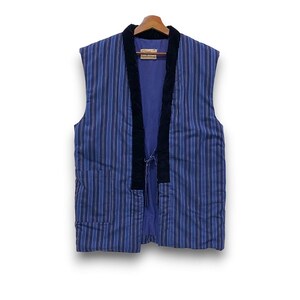 May include: A sleeveless vest featuring a blue and purple vertical striped pattern with a solid black velvet-textured trim along the front opening. The garment includes a small tie closure at the center and a visible interior label at the neck.