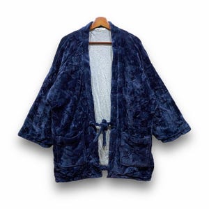 May include: A navy blue plush robe with a tie closure and two front pockets. The robe is made of a soft, textured material and hangs on a wooden hanger. The robe is open in the front, revealing a gray lining.