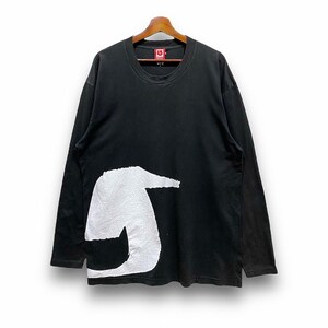 Puede incluir: Camiseta negra de manga larga con un gran gr&aacute;fico blanco en la parte delantera. La camiseta tiene cuello redondo y est&aacute; colgada de una percha de madera. La camiseta tiene una etiqueta con un cuadrado rojo y una letra blanca en su interior.