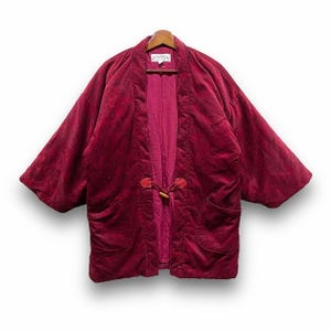 Könnte beinhalten: Burgunderfarbene Samtjacke mit lockerer Passform und kontrastierendem Innenfutter. Die Jacke hat einen Knebelverschluss aus Holz und zwei Vordertaschen. Das Etikett am Kragen lautet "AIGLON".