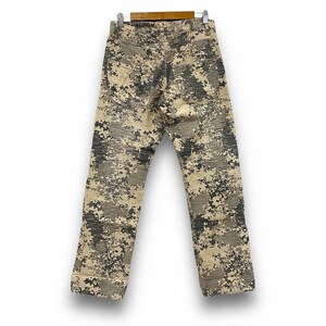 May include: Camouflage trousers in shades of beige, grey, and black, hanging on a wooden hanger. The trousers feature a digital camouflage design, with a straight-leg cut. The fabric appears to be a medium-weight material.