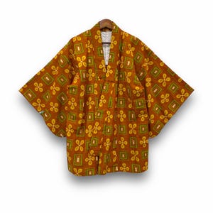 Peut inclure: Un kimono marron avec un motif géométrique de carrés et de formes florales jaunes et vertes. Le kimono est suspendu à un cintre en bois, mettant en valeur son devant ouvert et ses larges manches. Le tissu semble léger.