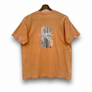 May include: Orange t-shirt with a surfboard graphic on the back. The graphic features a black and white surfboard, white flowers, and the text "Body Glove". The shirt is hanging on a wooden hanger.