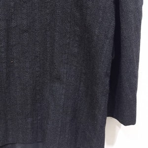 Op de afbeelding: Een donkergrijze blazer met een textuur in de stof. De blazer heeft een enkele knoopsluiting en lange mouwen.