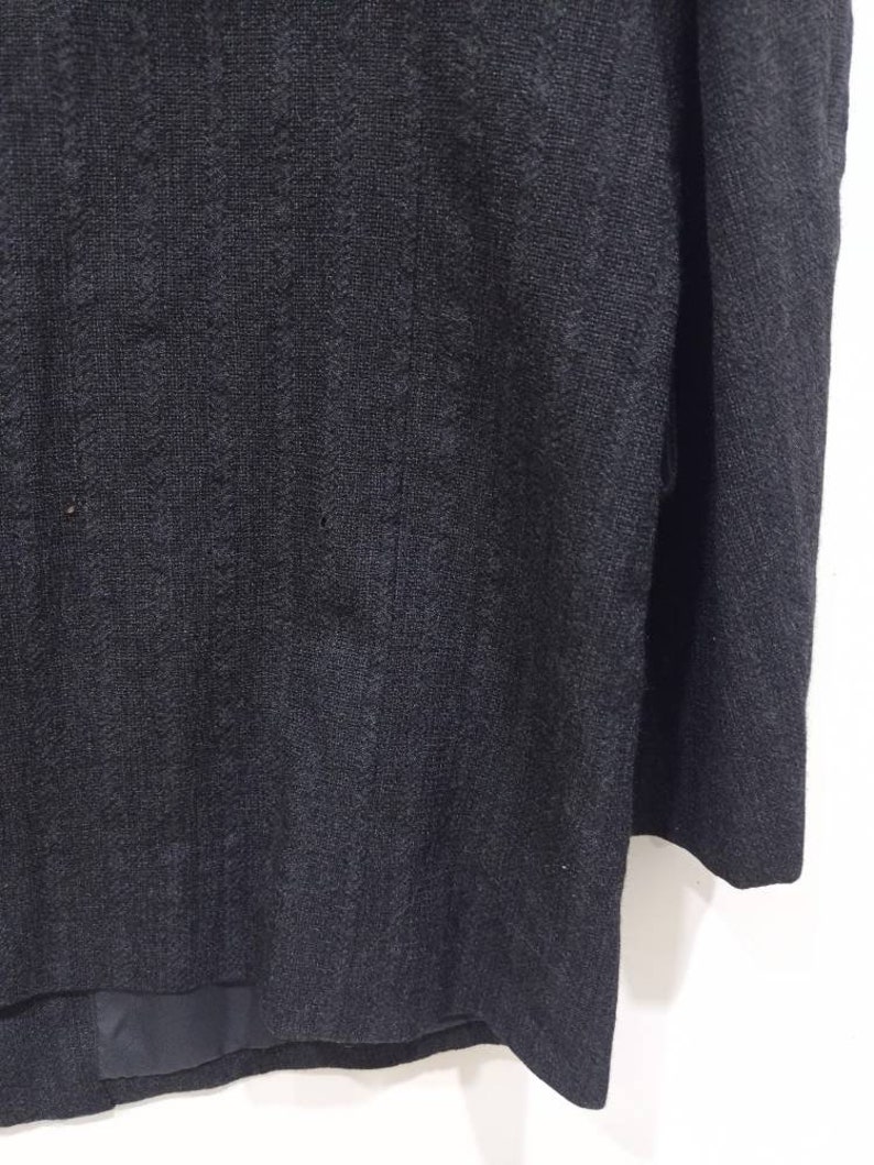 Op de afbeelding: Een donkergrijze blazer met een textuur in de stof. De blazer heeft een enkele knoopsluiting en lange mouwen.