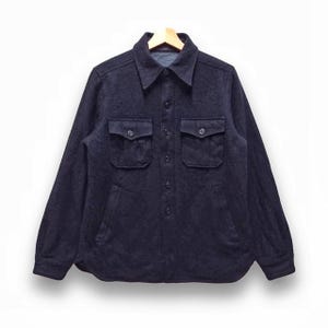 Puede incluir: Una camisa de manga larga azul oscuro con cierre de botones y dos grandes bolsillos de solapa. La camisa está hecha de una tela suave y texturizada.