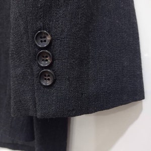 Op de afbeelding: Een zwart blazer met een textuur in de stof en drie knopen op de manchet.