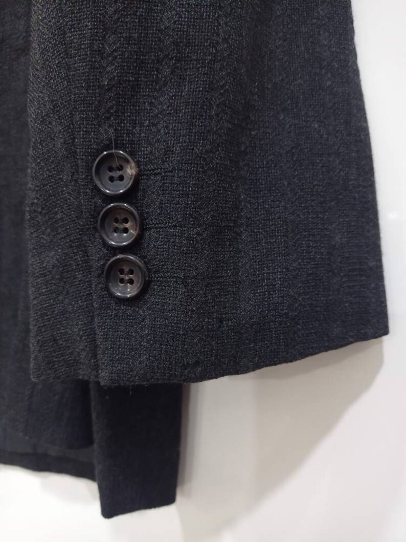 Op de afbeelding: Een zwart blazer met een textuur in de stof en drie knopen op de manchet.