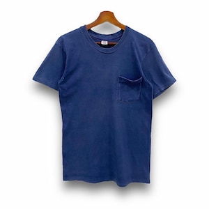 May include: A navy blue short-sleeved t-shirt with a chest pocket. The shirt is hanging on a wooden hanger against a white background. The t-shirt has a crew neck and a relaxed fit.