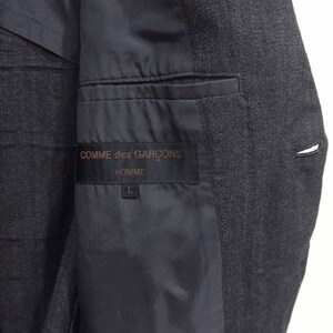 Op de afbeelding: Een zwart blazer met een zwarte voering en een label met de tekst "COMME des GAR&Ccedil;ONS HOMME" met maat L.