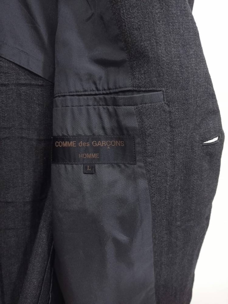 Op de afbeelding: Een zwart blazer met een zwarte voering en een label met de tekst "COMME des GAR&Ccedil;ONS HOMME" met maat L.