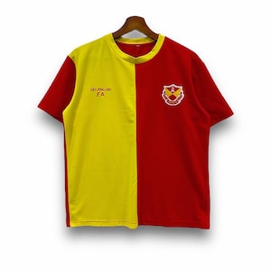 May include: A short-sleeved, two-toned t-shirt. The left side is yellow, and the right side is red. The shirt has a crew neck and features the text "SELANGOR FA" on the left side and a crest on the right side.