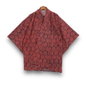 Peut inclure: Un kimono rouge avec un motif en nid d'abeille noir, suspendu à un cintre en bois. Le kimono est fait d'un tissu léger et a des manches larges. Le motif est un motif géométrique répétitif.