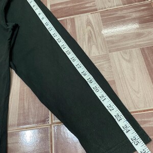 Puede incluir: Camiseta negra de manga larga, con una manga que mide 66 cm. La camiseta es de tela oscura y se mide con una cinta m&eacute;trica blanca. La camiseta est&aacute; sobre una superficie embaldosada.