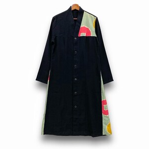 Peut inclure: Longue chemise noire boutonnée à manches longues. La chemise présente un col en V et un panneau décoratif sur l'épaule droite et le côté gauche. Le panneau est vert clair avec des motifs circulaires rouges, jaunes et blancs.
