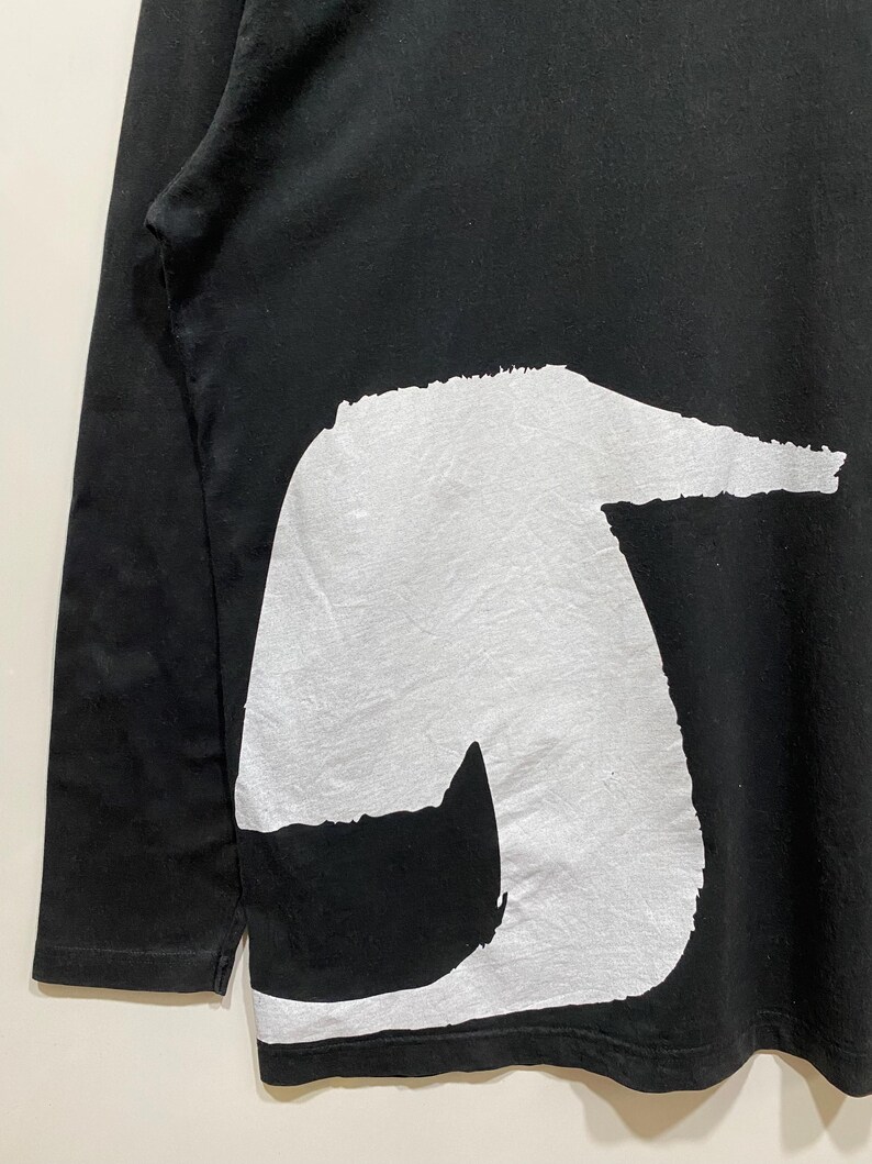 Puede incluir: Camiseta negra de manga larga con un gran dise&ntilde;o abstracto blanco en la parte delantera. El dise&ntilde;o tiene un aspecto texturizado. Las mangas son largas y la tela parece suave.