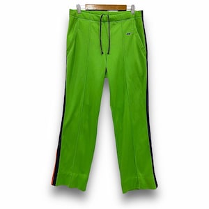 May include: Bright green athletic trousers with a drawstring waist and a small logo. The trousers have a navy blue stripe with a thin orange stripe down the side. The trousers are hanging on a wooden hanger.