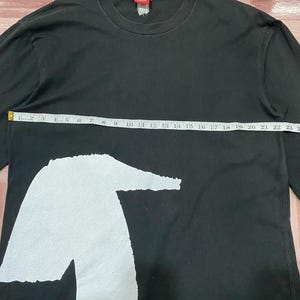 Puede incluir: Camiseta negra de manga larga con un gran gr&aacute;fico blanco. La camiseta mide 58 cm de ancho. Tiene cuello redondo y una etiqueta en la nuca.