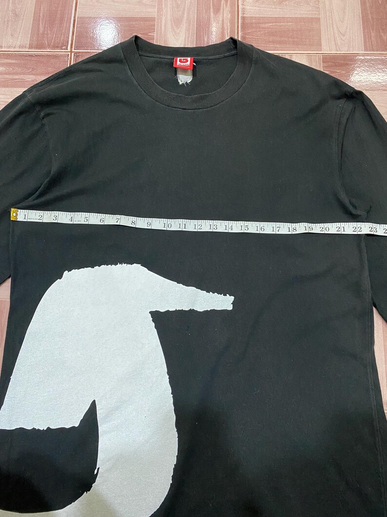 Puede incluir: Camiseta negra de manga larga con un gran gr&aacute;fico blanco. La camiseta mide 58 cm de ancho. Tiene cuello redondo y una etiqueta en la nuca.
