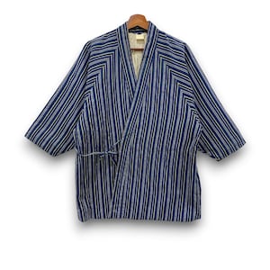May include: A blue and white striped jacket with a wrap-front design, wide sleeves, and a tie closure at the side. The garment features a V-neckline and a light-colored interior lining, presented on a wooden hanger against a plain background.