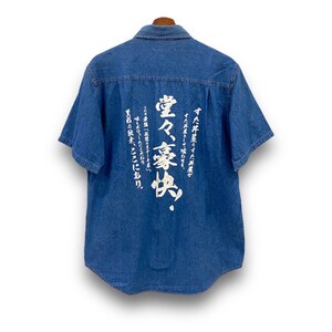 May include: A blue denim short-sleeved shirt with white Japanese calligraphy on the back. The text reads: "すた丼屋のすた丼屋がすた丼屋として喰わせる、堂々豪快『伝説のステーキ屋』味とボリュームにこだわり至石の絵を、ここにあり。"