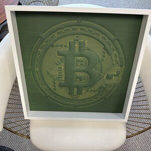 May include: A framed green canvas with a yellow embroidered Bitcoin logo. The logo is a stylized letter B with circuit board designs.