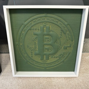 May include: A framed green fabric artwork with a yellow embroidered Bitcoin symbol.