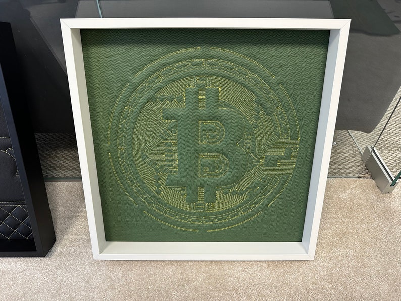 May include: A framed green fabric artwork with a yellow embroidered Bitcoin symbol.