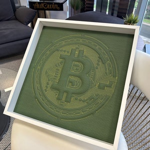 May include: A white framed square canvas with a green background and a yellow embroidered Bitcoin symbol.
