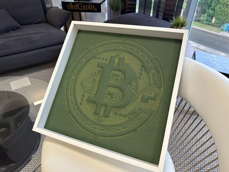 May include: A white framed square canvas with a green background and a yellow embroidered Bitcoin symbol.