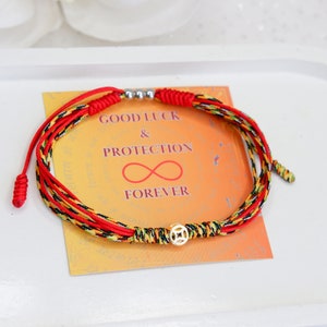 May include: Red, yellow, and black braided string bracelet with a gold charm and silver beads. The bracelet is on a card that says "Good Luck & Protection Forever".