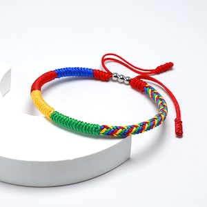 May include: A colorful braided bracelet with red, yellow, blue, and green threads. The bracelet has silver metal beads and a braided closure.