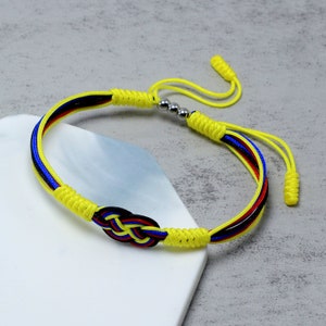 Op de afbeelding: Een gevlochten armband in geel, blauw en zwart met een knoop in het midden. De armband heeft zilveren metalen kralen.