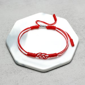 May include: Red and white string bracelet with a silver bead and a knot in the center.