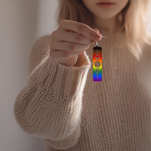 May include: Rainbow colored dangle earrings with a crescent moon design. The earrings are made of metal and have a silver hook.