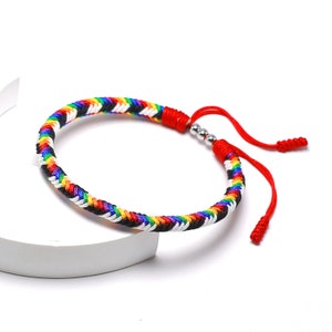 May include: A colorful braided bracelet with a red cord and silver beads. The bracelet is made of rainbow colored string and has a black and white pattern.