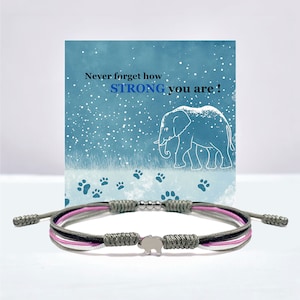 May include: A grey, pink and white braided bracelet with a silver elephant charm. The bracelet comes with a card that reads "Never forget how STRONG you are!" with a drawing of an elephant in a snowy landscape.
