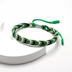 Puede incluir: Un brazalete trenzado verde, negro, blanco y verde oliva con un acento de cuentas plateadas.