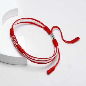 May include: Red and white braided bracelet with silver beads. The bracelet has a knot at each end.