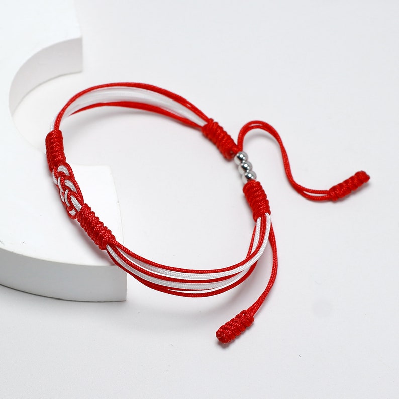May include: Red and white braided bracelet with silver beads. The bracelet has a knot at each end.