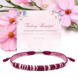 May include: A pink and white string bracelet with a sliding knot closure. The bracelet has a woven design with silver beads. A card behind the bracelet reads "Fucking Beautiful" and "morse code protection string bracelet".