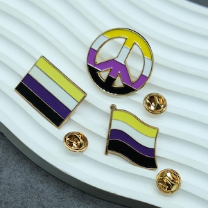 Könnte beinhalten: Vier goldfarbene Pins mit einem Friedenszeichen, einer Flagge und zwei Rückseiten. Das Friedenszeichen ist gelb, weiß, lila und schwarz. Die Flagge ist gelb, weiß, lila und schwarz. Die Rückseiten sind golden.
