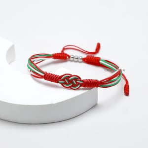 Könnte beinhalten: Geflochtenes Armband aus roter, weißer und grüner Schnur mit einem Knotendesign und silbernen Perlen.