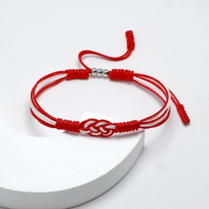 May include: Red and white braided string bracelet with a silver knot and beads.