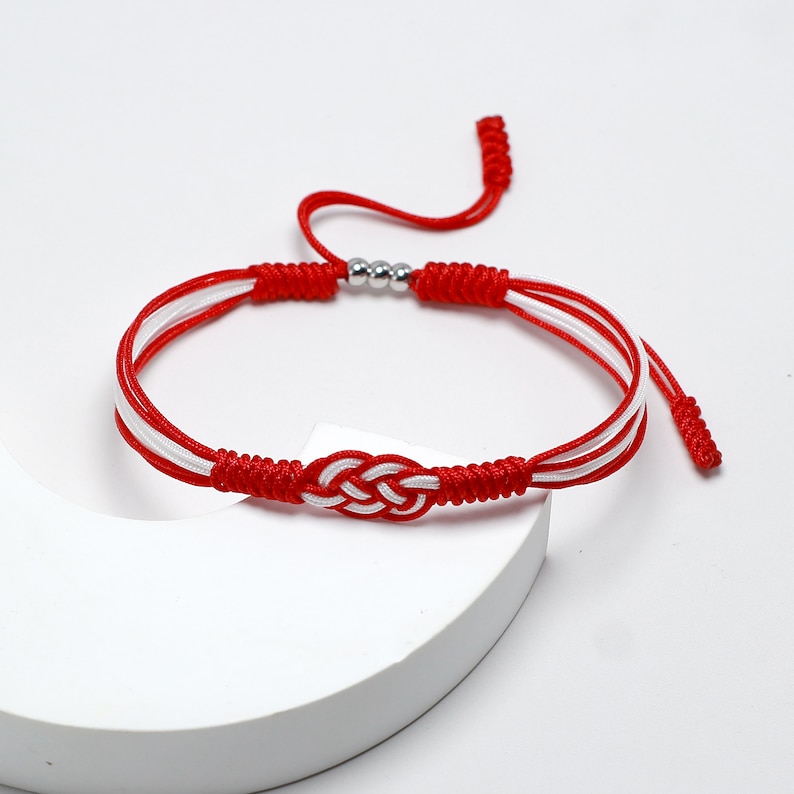 May include: Red and white braided string bracelet with a silver knot and beads.