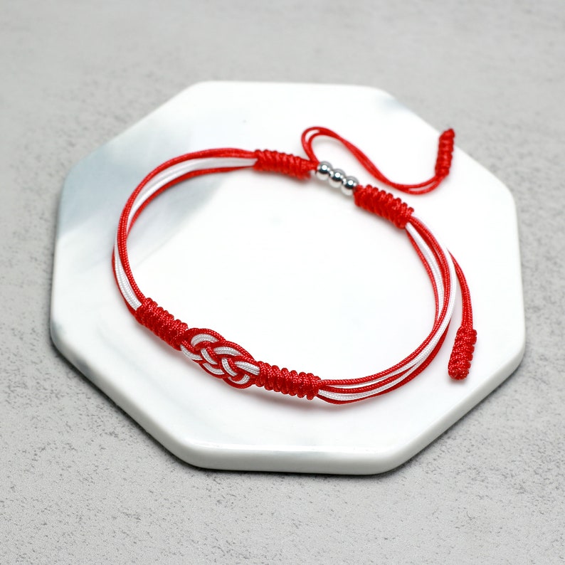May include: Red and white braided bracelet with silver beads and a knot design.